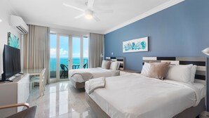 A hotel room with two beds, a TV, a desk, and a balcony with a view of the sea. - Waterside Historic District Sweeping Views (San Juan)