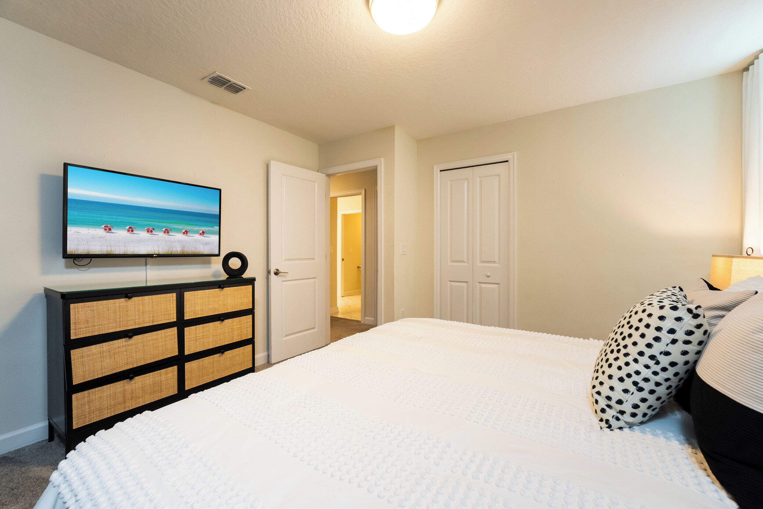 A bedroom with a bed, a dresser, a television on the wall, and a door leading to another room.
