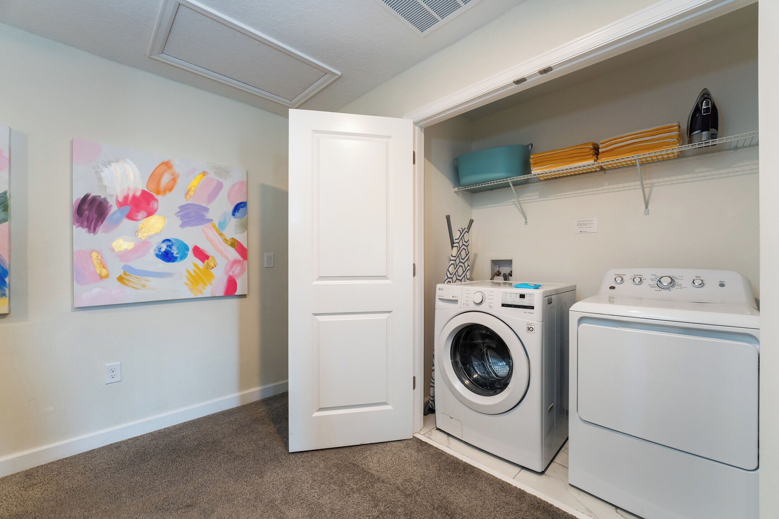 A laundry room with a washing machine, dryer, and shelves with folded towels and a basket.