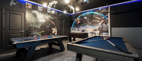 Une table de billard recouverte d’un drap bleu, deux tables de baby-foot et un écran de projection diffusant une image sur le thème de l’espace.