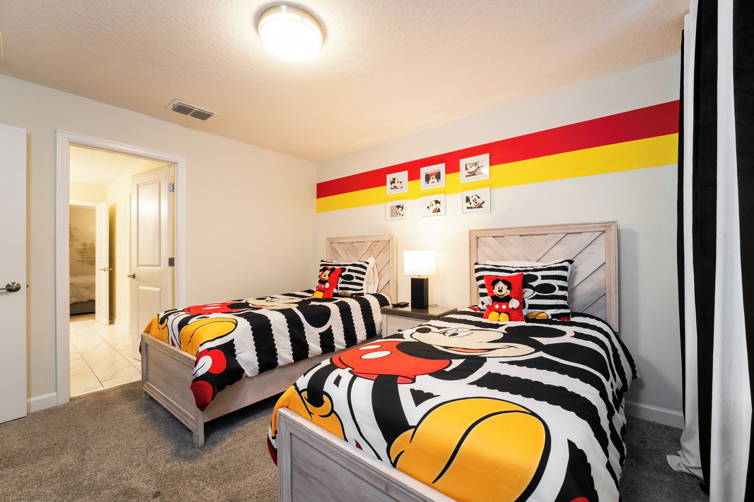 A bedroom with two beds, each with Mickey Mouse themed bedding, a door leading to another room, and a wall with framed pictures.