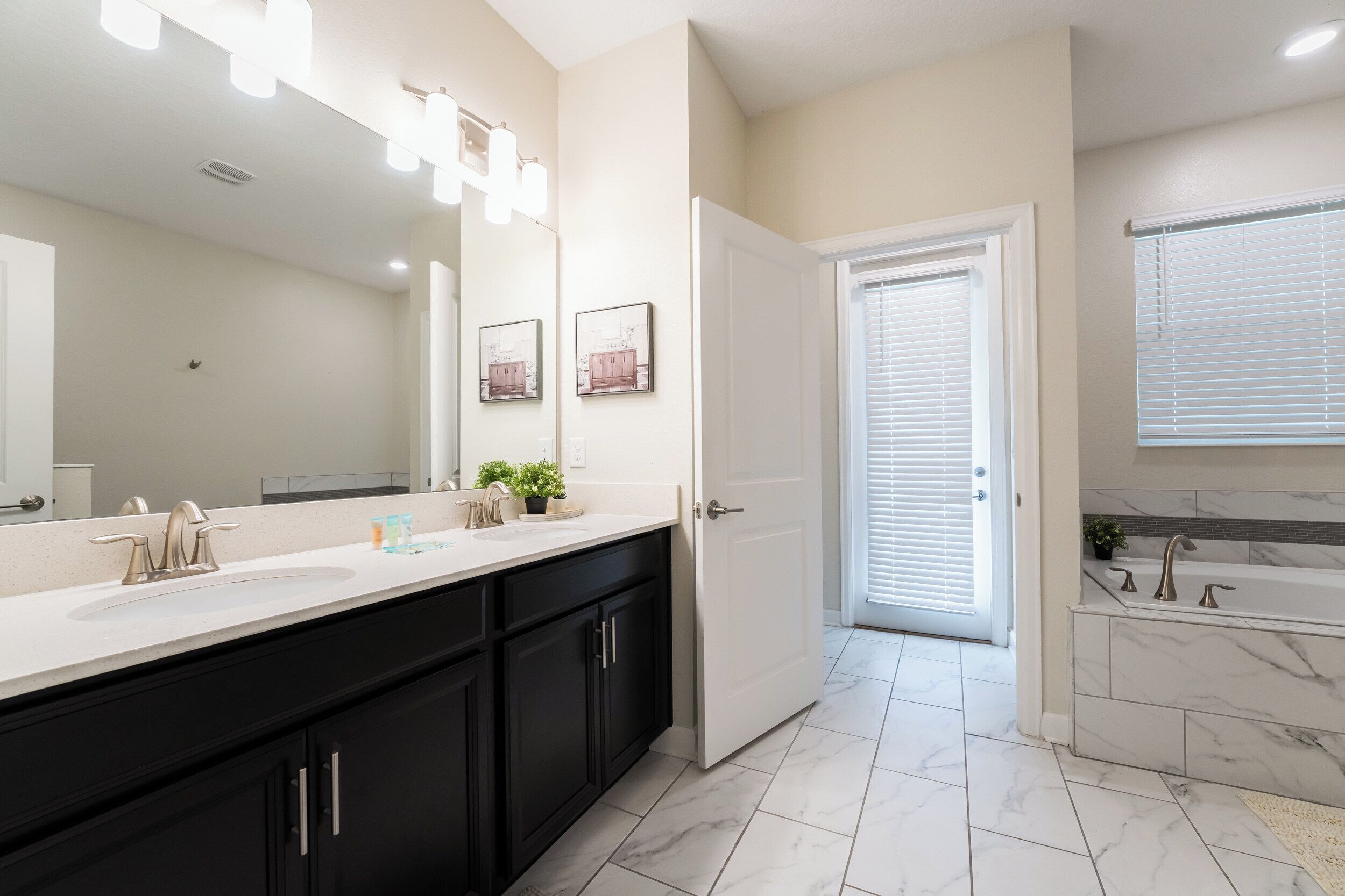 A modern bathroom with a large mirror, a double sink, and a bathtub.