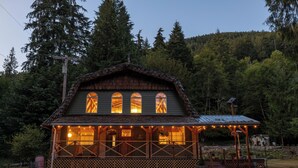 A rustic cabin with a porch, large windows, and a small attached structure with a roof.