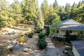 A house surrounded by a forested area with a stone pathway leading to a deck. - Sleeps 24 • Forest • Sauna • Massage Chair (Eugene)