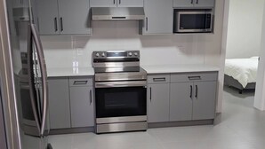 A modern kitchen with stainless steel appliances, grey cabinets, and a microwave. - Fully Furnished Holiday Rental 02 BR Suite (Surrey)