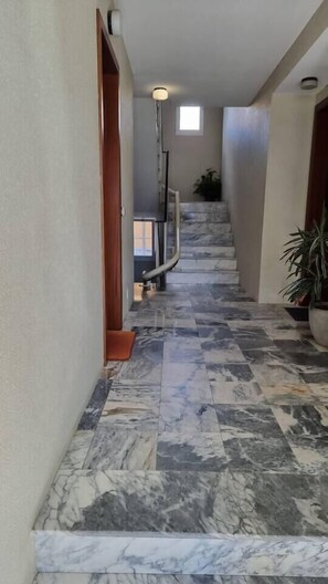 Ein Korridor mit Marmorboden, Holztüren und einer Treppe, die in ein Obergeschoss führt.
