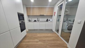 Kompakti keittiö, jossa on valkoiset kaapit, sisäänrakennettu uuni ja kahvinkeitin.