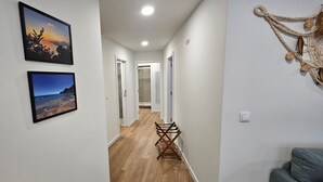 Un pasillo con suelo de madera, paredes blancas y dos cuadros enmarcados. En el centro hay una pequeña mesa con una silla.
