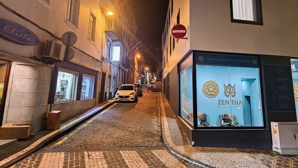 Uma rua de paralelepípedos estreita à noite, com edifícios em ambos os lados, incluindo um centro de terapia de massagem.