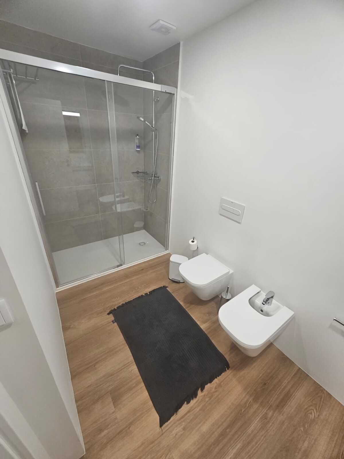 A modern bathroom with a glass-enclosed shower, a toilet, and a sink.