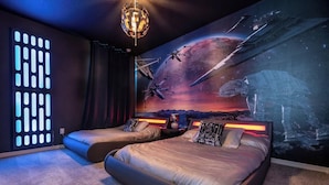 Une chambre avec deux lits, une fresque murale représentant des œuvres d’art sur le thème de l’espace, et un luminaire moderne.