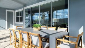 Une terrasse extérieure avec une table rectangulaire et six chaises, entourée de grandes baies vitrées.