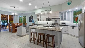 A modern kitchen with a central island, bar stools, and a dining area with chairs. - Oceanfront Villa, Private Pool, Great Sunsets (Cozumel)