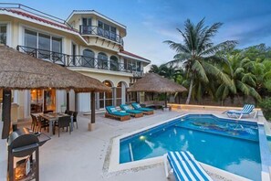 A poolside area with a pool, lounge chairs, and a dining area with a table and chairs. - Oceanfront Villa, Private Pool, Great Sunsets (Cozumel)