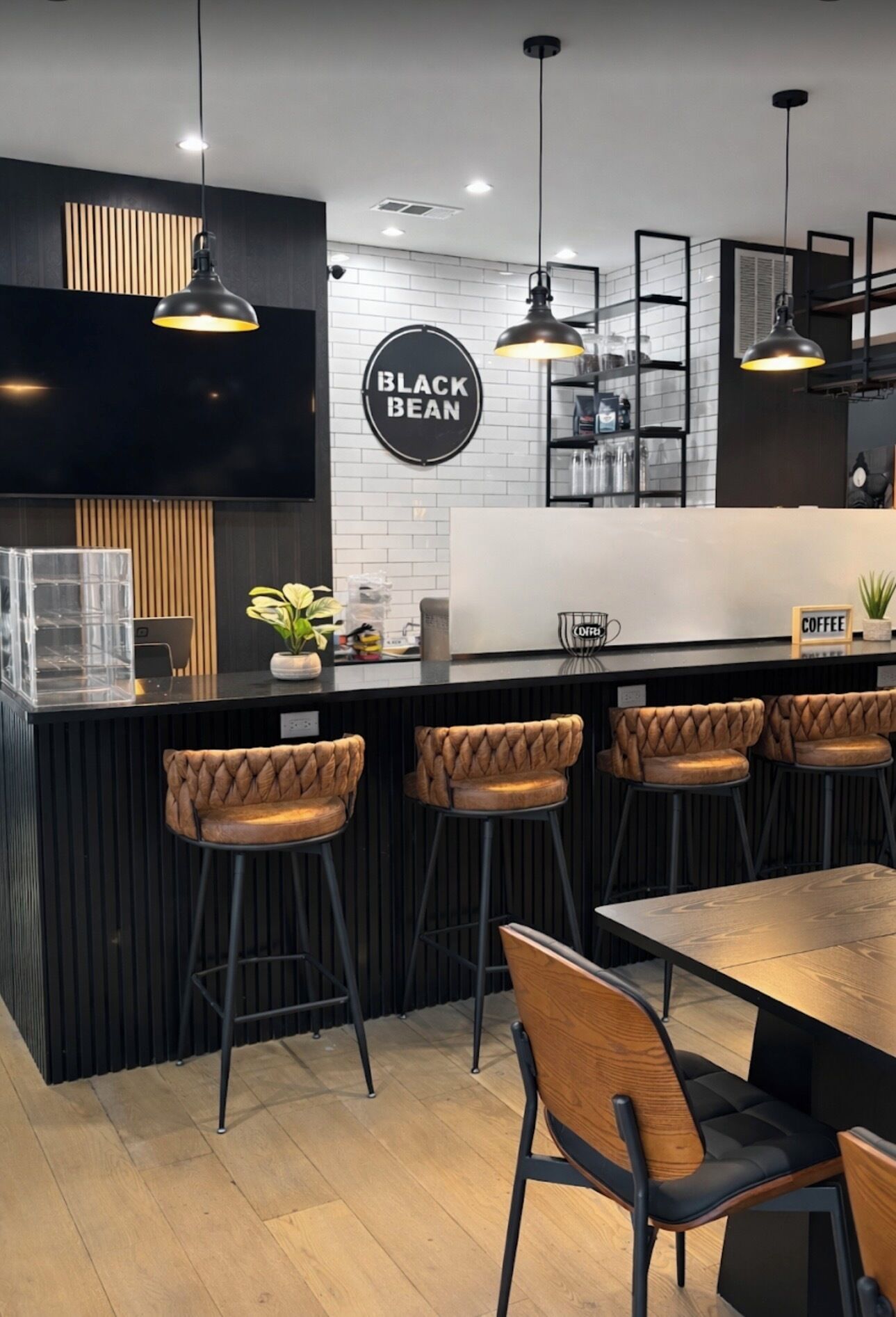 A modern bar area with a wooden counter, black bar stools, and a sign reading 'BLACK BEAN'.