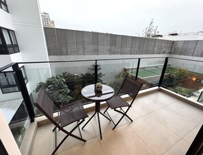A balcony with a glass railing, two chairs, a small round table, and potted plants.