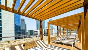A rooftop lounge with sun loungers and a view of city buildings. - First Line Canal View Studio w/ Balcony MAX 4 Pax (Dubai Marina)