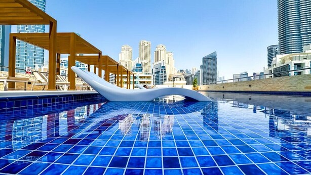 A swimming pool with a cityscape view, wooden pergola, and a white floating structure. - First Line Canal View Studio w/ Balcony MAX 4 Pax (Dubai Marina)
