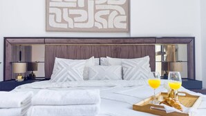 A neatly made bed with white linens, a tray with croissants and juice glasses, and a large abstract artwork on the wall. - UltraLuxury Flat Amazing Pool Near to Burj Al Arab (Jumeirah Medinat Living)