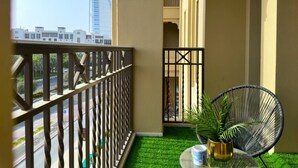 Un balcon donnant sur un immeuble de grande hauteur, avec une balustrade, une chaise et une petite table agrémentée d’une plante.