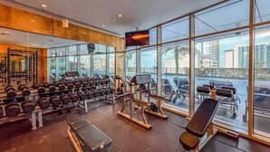 Une salle de sport équipée de matériel d’exercice, dotée de grandes fenêtres et offrant une vue sur la ville.