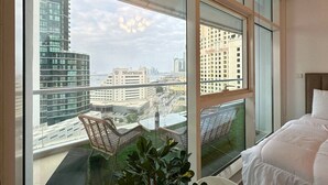 A modern hotel room with a large balcony, a bed, and a view of the cityscape. - Opulent Flat with Beach, Pool & Canal View in JBR (Dubai Marina)