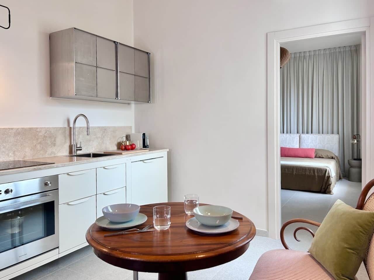 Een compacte hotelkamer met een kitchenette, een eettafel met kommen en glazen, en een bed met gordijnen.