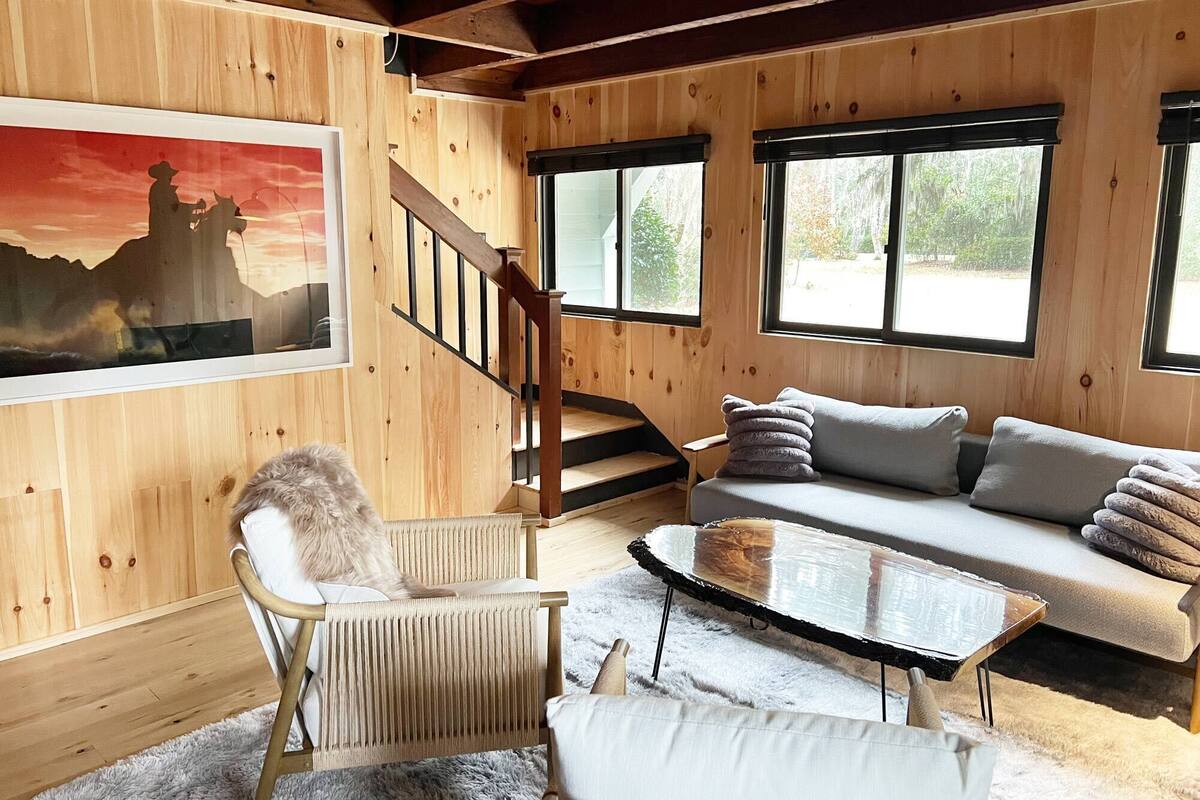 L’intérieur chaleureux d’un chalet, avec un revêtement mural en bois, un canapé, un fauteuil, une table et un escalier.