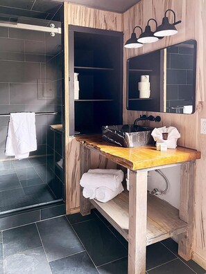 A modern bathroom with a wooden vanity, a glass shower enclosure, and a mirror with lights.