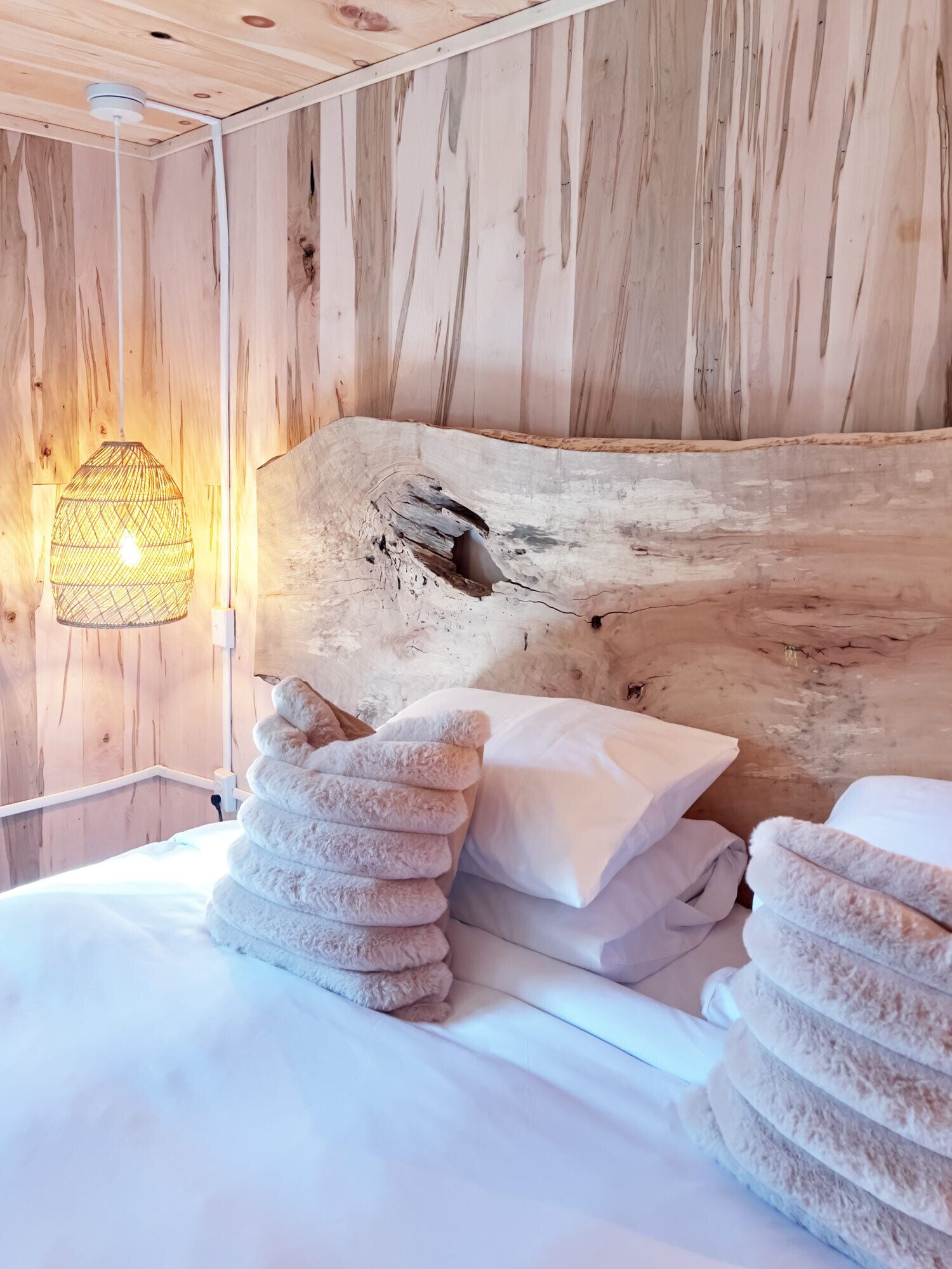 Une tête de lit en bois à la texture originale, un lit avec du linge de lit blanc et un luminaire suspendu.