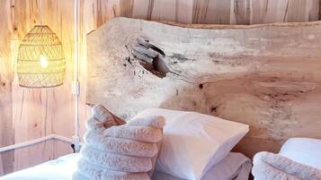 Une tête de lit en bois à la texture originale, un lit avec du linge de lit blanc et un luminaire suspendu.