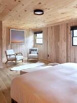 Una habitación con una cama grande, dos sillones, un cuadro y un ventanal.