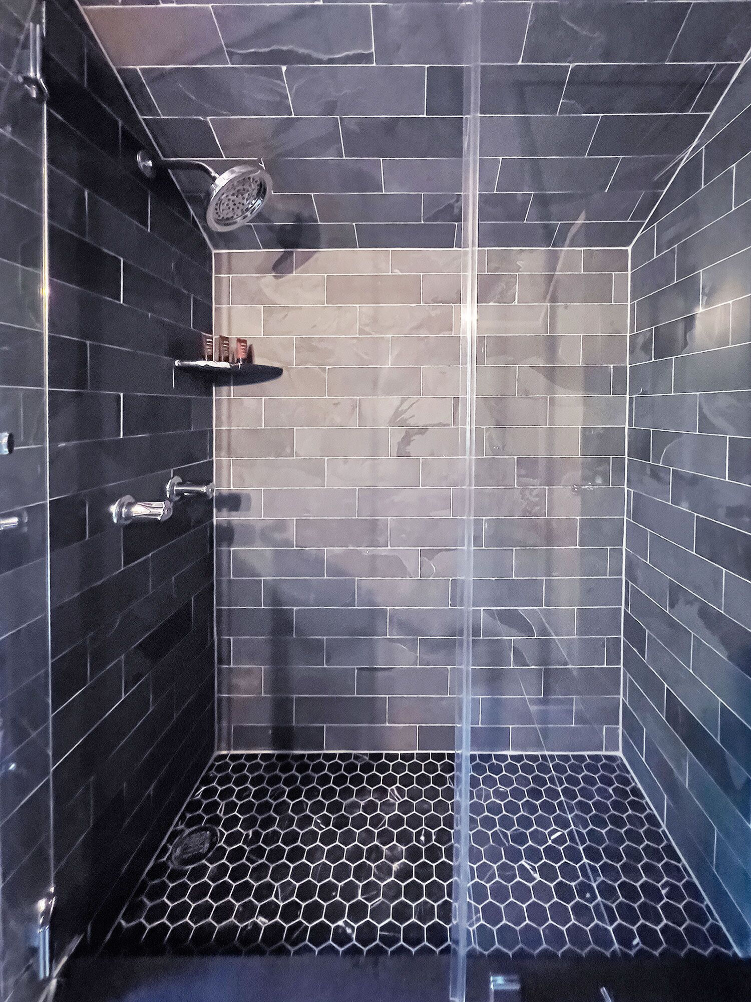 A modern shower with a glass door, a metal showerhead, and a tiled floor with a hexagonal pattern.