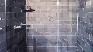A modern shower with a glass door, a metal showerhead, and a tiled floor with a hexagonal pattern.