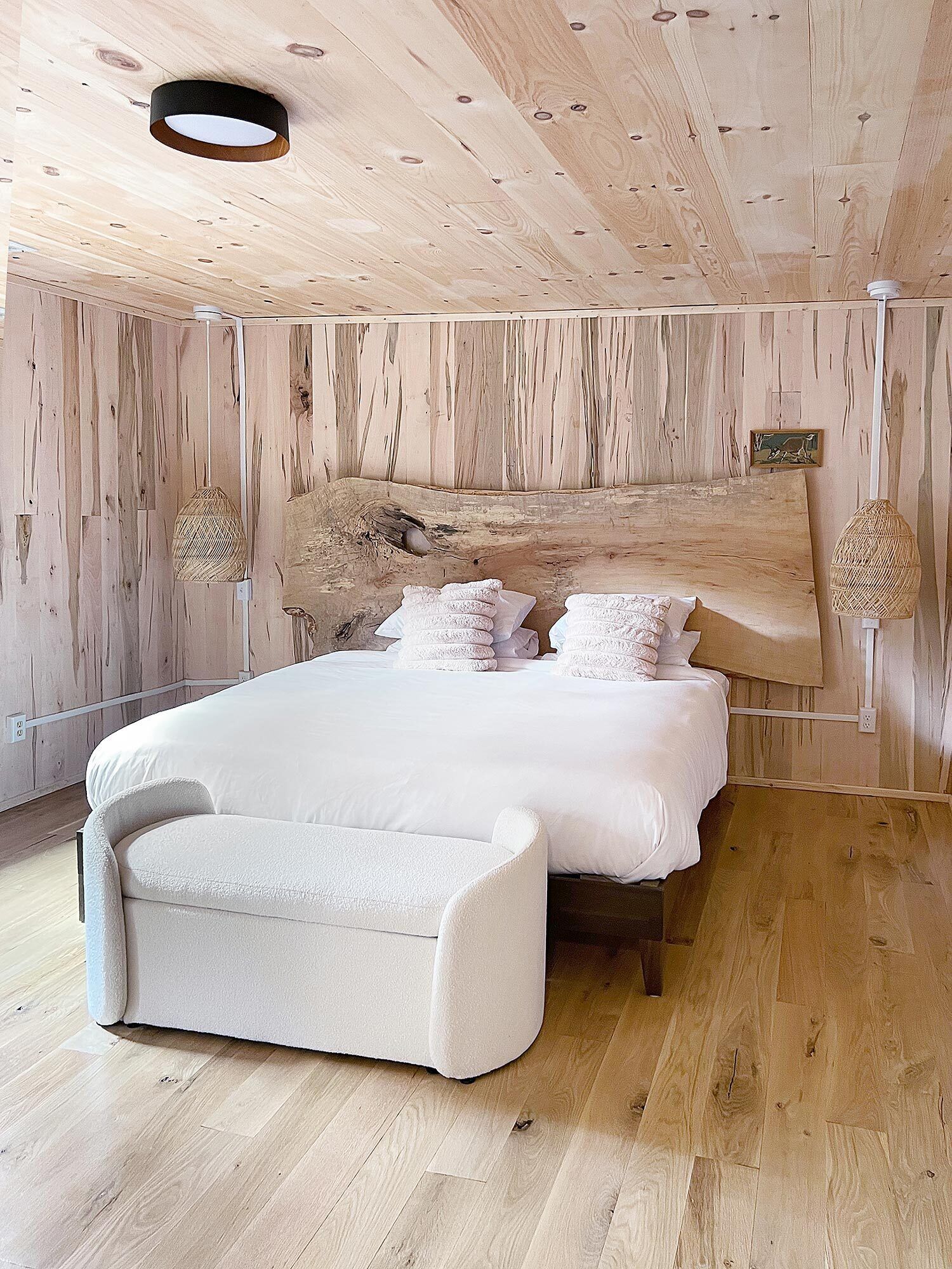 Een slaapkamer met een groot bed, een bankje, houten wanden en een plafondlamp.
