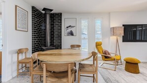 A modern dining area with a round wooden table, six wooden chairs, a yellow armchair, and a black and white brick wall. - Slow M’Ocean Cabarita - Pet Friendly (Tweed)
