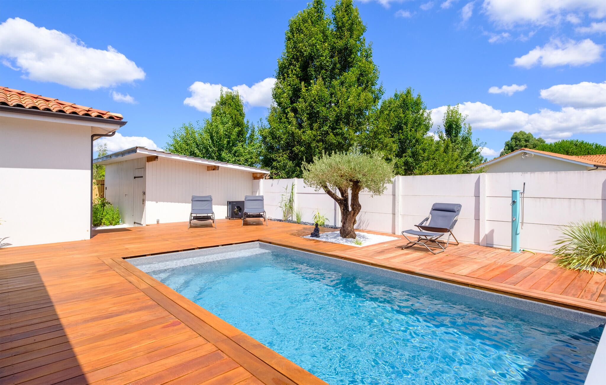 A swimming pool with wooden deck, two lounge chairs, and a tree.