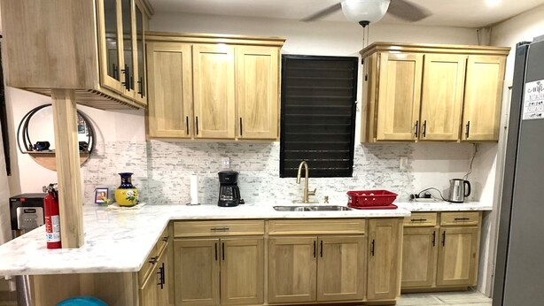 A kitchen with wooden cabinets, a marble countertop, a sink, a coffee maker, and a red fruit basket.