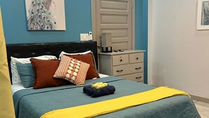 A bedroom with a bed, pillows, a bedside table, a door, and a painting on the wall.