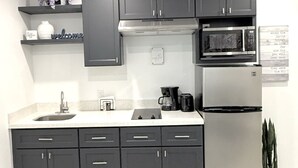 Eine moderne Küche mit dunkelgrauen Schränken, einem Edelstahl-Kühlschrank, einer Mikrowelle und einer Kaffeemaschine.