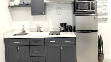 Una cocina moderna con armarios oscuros, un refrigerador de acero inoxidable, un microondas y una cafetera.