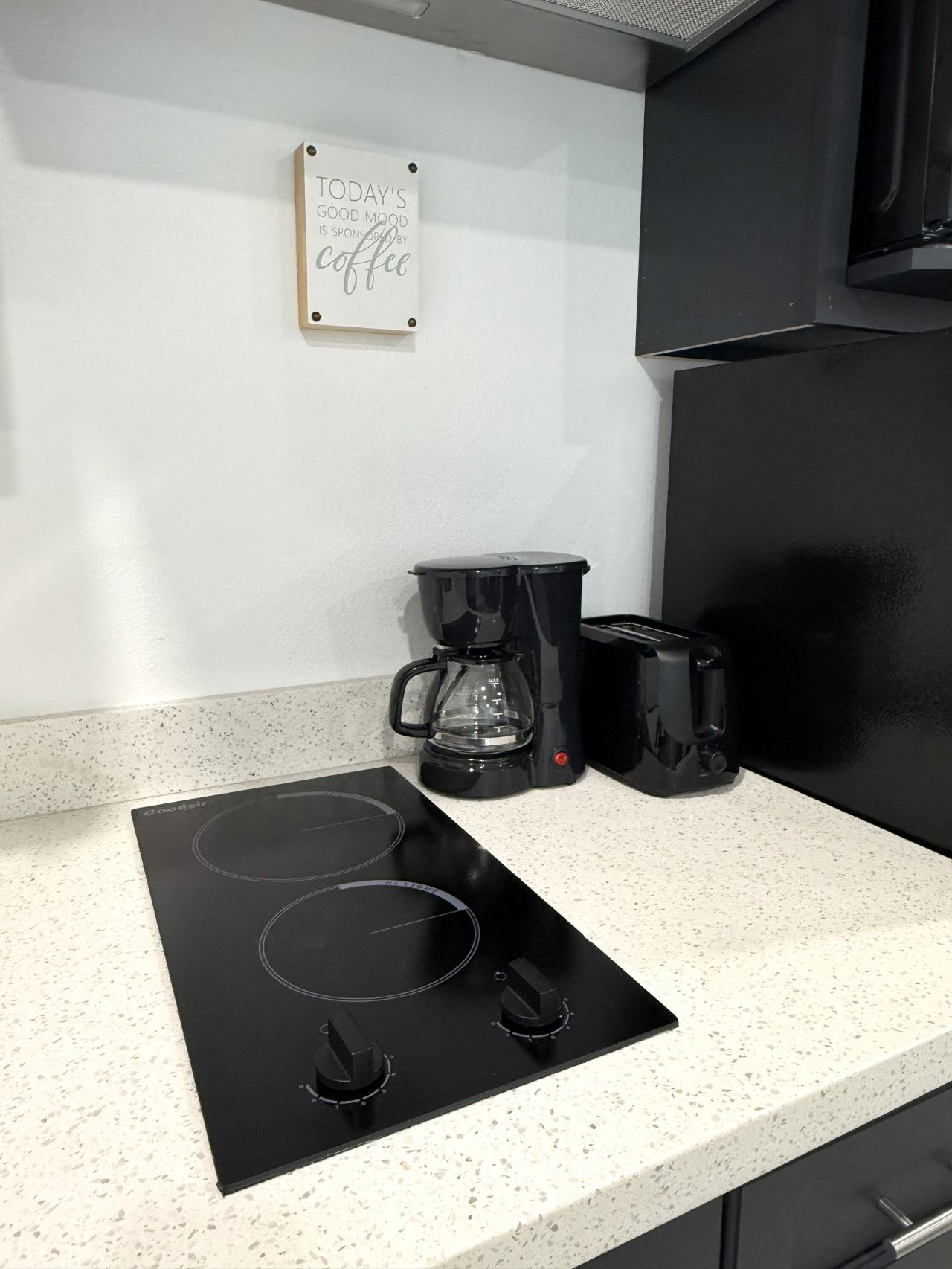 A kitchen with a black induction cooktop, a coffee maker, and a toaster on a speckled countertop.