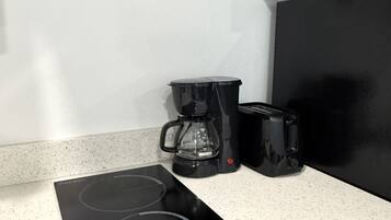 A kitchen with a black induction cooktop, a coffee maker, and a toaster on a speckled countertop.