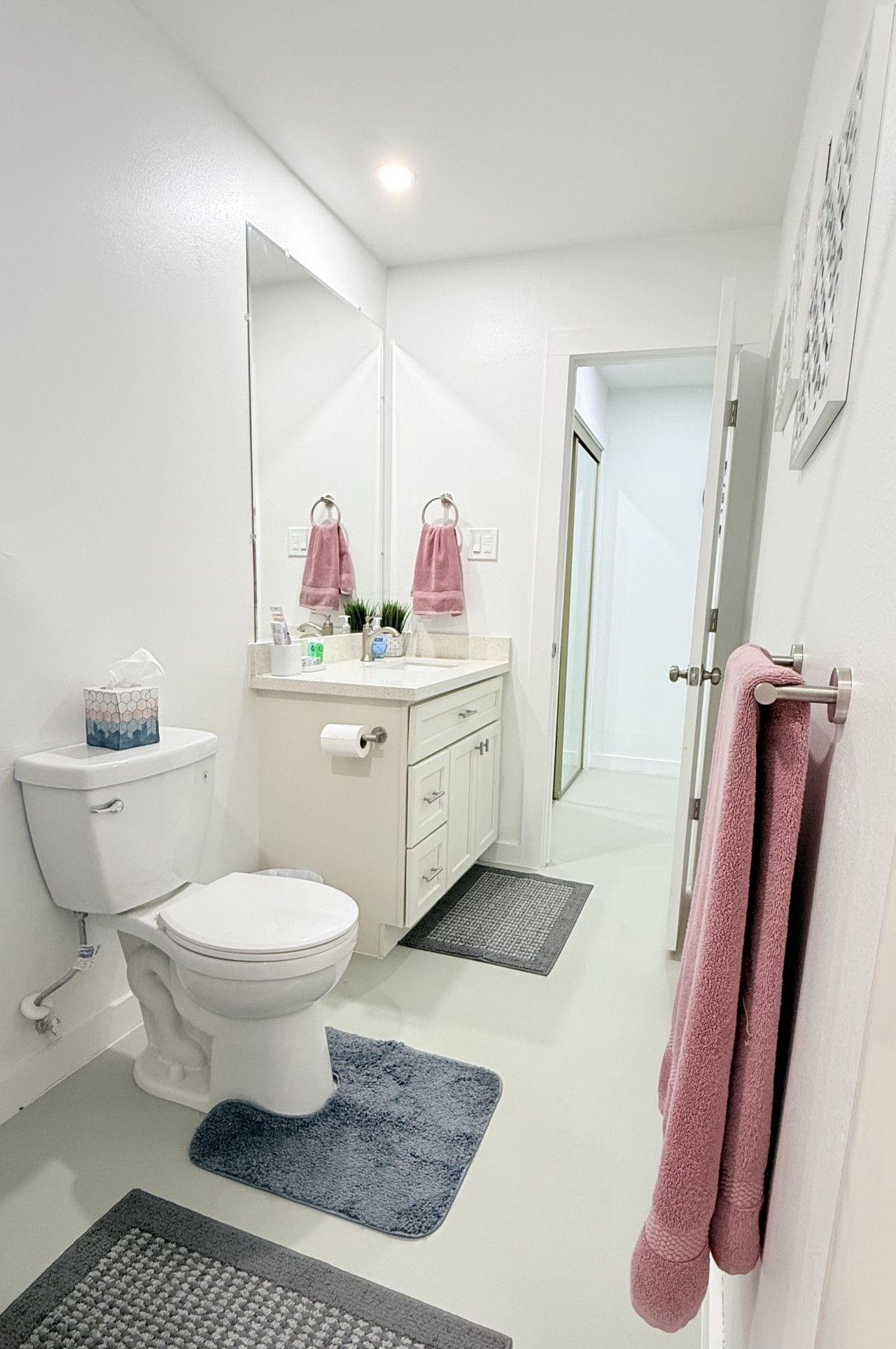 Ein modernes Badezimmer mit Toilette, Waschbecken und Spiegel. Zwei Handtücher hängen an der Wand und ein Teppich liegt auf dem Boden.