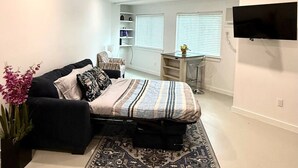 Ein modernes Schlafzimmer mit einem Bett, einer schwarzen Couch, einem Fernseher und einem Schreibtisch.