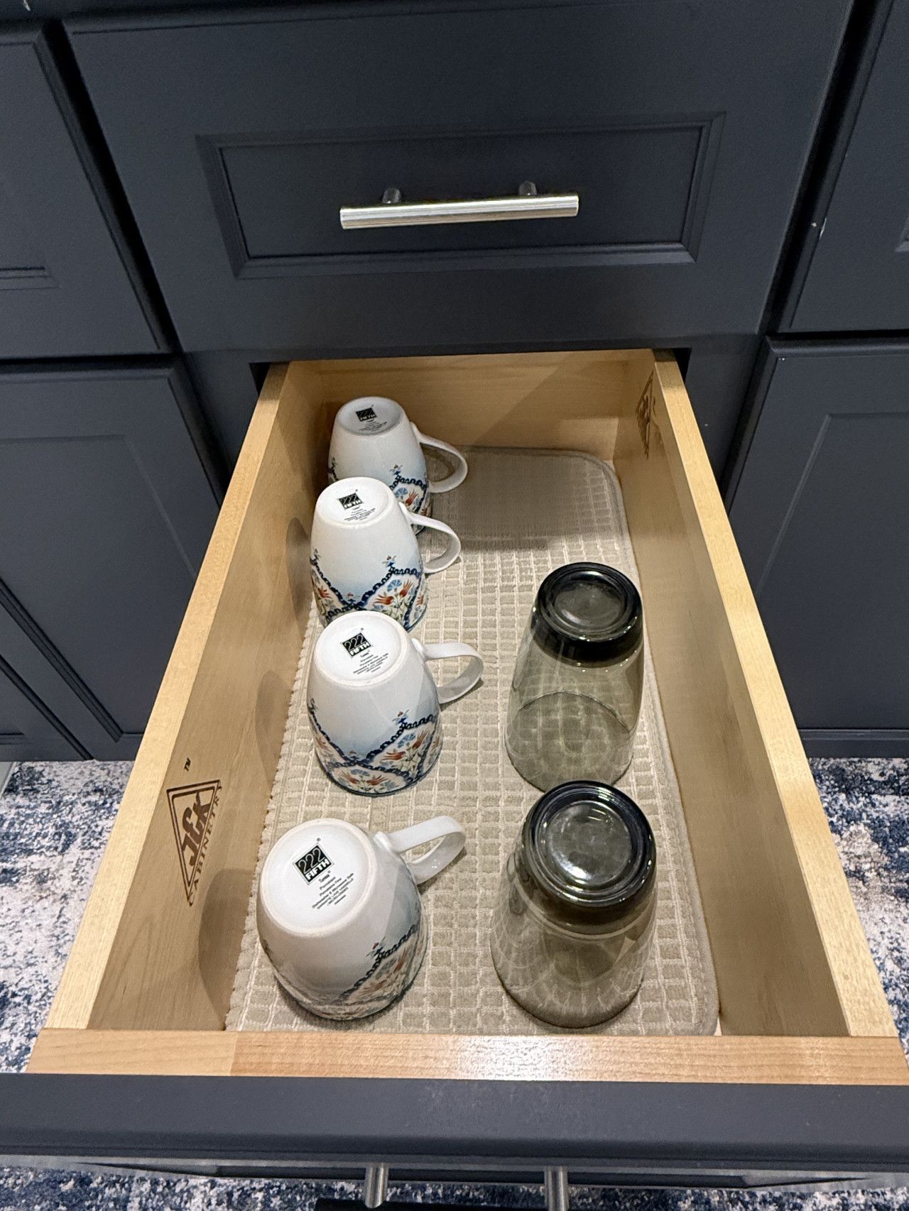 Un tiroir contenant quatre tasses en céramique blanche ornées de motifs floraux, deux bocaux en verre transparent et un plateau en bois.