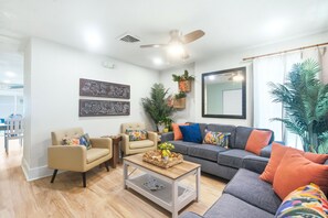 Una sala de estar con un sofá gris, sillones color beige, una mesa de centro y un ventilador de techo.