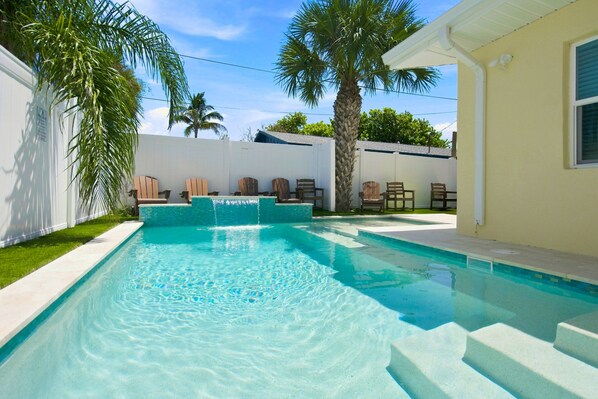 A rectangular swimming pool with a clear blue water surface, surrounded by a white wall and a small grassy area.