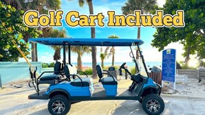 A golf cart with a blue canopy parked on a paved area with palm trees and a beach in the background.