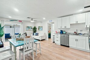A modern kitchen with white cabinets, a dishwasher, and a dining area with a table and chairs.